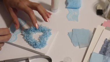 Masadaki kadın bir tebrik kartı yapıyor. Kağıt elementleri gül şeklinde yapıştırır. Cihazlar ve malzemeler yakınlarda serili..