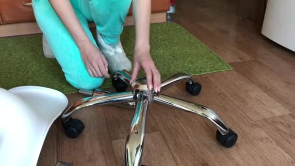The woman collects a computer chair on wheels. Installs the lifting mechanism into the crosspiece. Parts for the office chair are on the floor in the apartment. — Video Stock