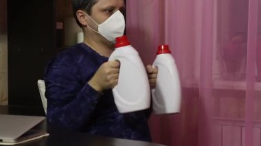 Tıbbi maskeli bir adam kendini izole ederek jimnastik yapar. Dambıl yerine konserve deterjan. Dambılları öne ve arkaya doğru itin..