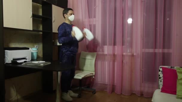 En man i medicinsk mask gör gymnastik i självisolering. Istället för hantlar, burkar med tvättmedel. Lyfthantlar för biceps stående. — Stockvideo