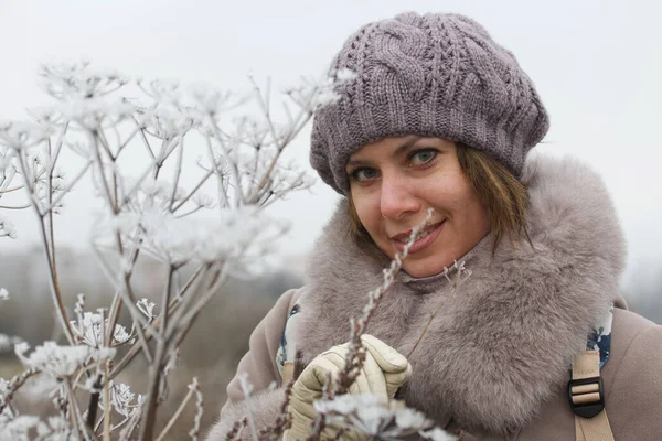 A woman in winter clothes walks in the park. Around the dried plants covered with ice crust and frost.