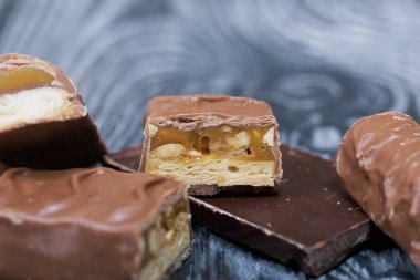 Doğranmış çikolata. Karamel ve fındık dolu. Yakınlarda çikolata parçaları var. Siyah çam tahtalarında.