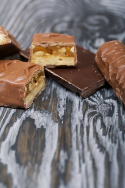 Doğranmış çikolata. Karamel ve fındık dolu. Yakınlarda çikolata parçaları var. Siyah çam tahtalarında.