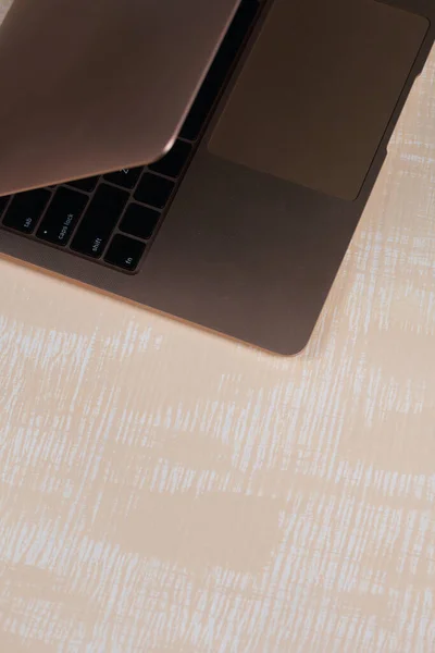 Fragment of an open pink laptop. The surface is painted in white and beige.