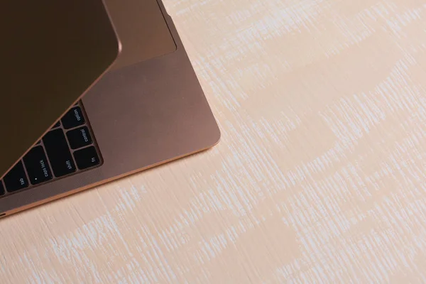 Fragment of an open pink laptop. The surface is painted in white and beige.