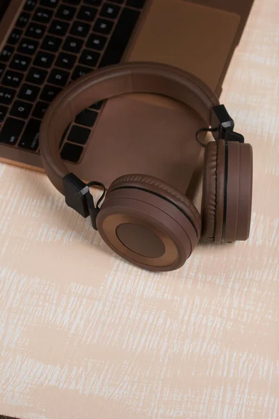 Fragment of an open pink laptop. Nearby are wireless headphones in brown. The surface is painted in white and beige.