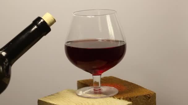 Ten muž dolévá víno. Červené víno ve skleněné číši. Stojí na dřevěných škytavkách. Otočí se na světlém pozadí. Detailní záběr. — Stock video