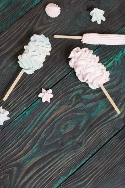 Zephyr on a stick. Nearby are marshmallow stars of different shades. Close-up shot. Against a background of black-green pine boards.