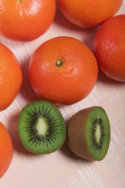 Birkaç portakal mandalinası. Kivi meyvesi ikiye bölünmüş. Sulu yeşil et görünür. Bej bir yüzeye uzan.