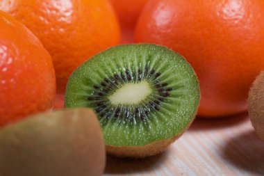 Birkaç portakal mandalinası. Kivi meyvesi ikiye bölünmüş. Sulu yeşil et görünür. Yakın plan çekim. Bej bir yüzeye uzan.