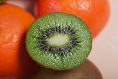 Birkaç portakal mandalinası. Kivi meyvesi ikiye bölünmüş. Sulu yeşil et görünür. Yakın plan çekim. Bej bir yüzeye uzan.