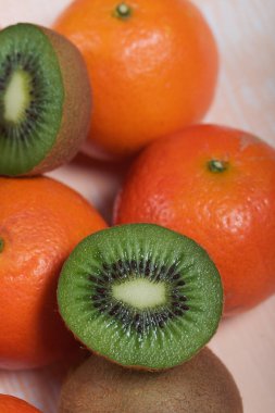 Birkaç portakal mandalinası. Kivi meyvesi ikiye bölünmüş. Sulu yeşil et görünür. Bej bir yüzeye uzan.
