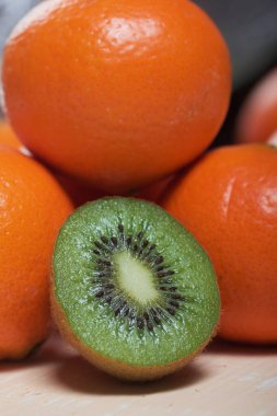 Birkaç portakal mandalinası. Kivi meyvesi ikiye bölünmüş. Sulu yeşil et görünür. Yakın plan çekim. Bej bir yüzeye uzan.