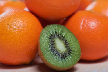 Birkaç portakal mandalinası. Kivi meyvesi ikiye bölünmüş. Sulu yeşil et görünür. Yakın plan çekim. Bej bir yüzeye uzan.