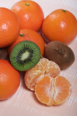 Turuncu mandalina. Kabuksuz bir tane. Kivi meyvesi ikiye bölünmüş. Sulu yeşil et görünür. Yakın çekim..