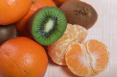 Turuncu mandalina. Kabuksuz bir tane. Kivi meyvesi ikiye bölünmüş. Sulu yeşil et görünür. Yakın çekim..