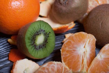 Turuncu mandalina. Kabuksuz bir tane. Kivi meyvesi ikiye bölünmüş. Sulu yeşil et görünür. Yakın çekim..