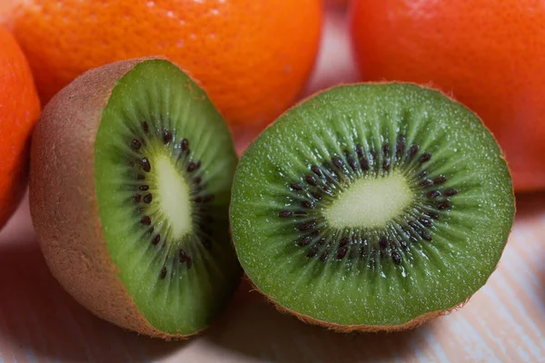 Birkaç portakal mandalinası. Kivi meyvesi ikiye bölünmüş. Sulu yeşil et görünür. Yakın plan çekim. Bej bir yüzeye uzan.