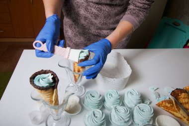 Lastik eldivenli kadın marşmelov yapıyor. Yakınlarda waffle külahında bir zephyr var. Tatlı masa yüzeyinde yatıyor..