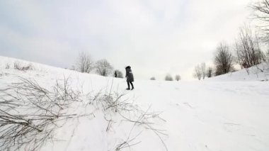 Kız karla kaplı bir tepeye tırmanıyor, bir kızağa biniyor ve tepenin dibine kayıyor..