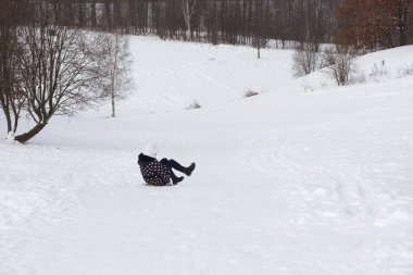 Kışın yürüyüşe çıkan genç bir kadın. Kış kıyafetleri içinde. Karda oturuyor. Etrafta çok kar var..