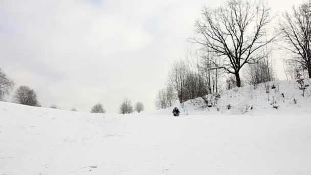 La ragazza sale su una collina innevata, si siede su una slitta e scivola verso il fondo della collina. cade da un lato e sale. — Video Stock