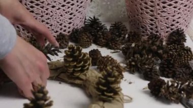 Bir kadın çam kozalağından bir çelenk topluyor. Karton ve kağıttan yapılmış bir yüzüğe koni takıyor. El sanatları için aksesuarları.