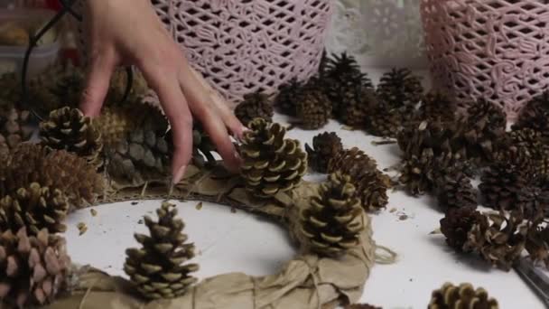 Uma mulher recolhe uma coroa de pinhas. Anexa cones a um anel feito de papelão e papel. Imagem de close-up. — Vídeo de Stock