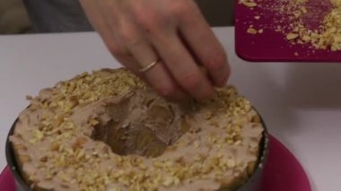 Kadın pastaya kavrulmuş fıstık serpiyor. Kremayla kaplı bisküvilerden yapılmış bir pasta.