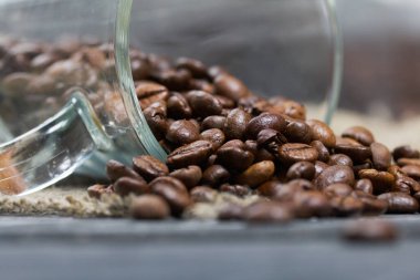 Kahve çekirdekleriyle çevrilmiş cam bardak. Kahve çekirdekleri keten ve çam ağaçlarına saçıldı. Yakın çekim..