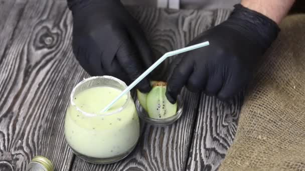 Een man versiert een kiwi milkshake met een kiwi plak. — Stockvideo