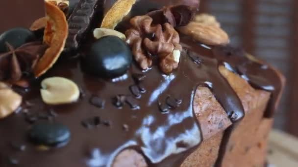 Banana bread garnished with melted chocolate, nuts and dried fruits. Rotates on the stage. Close-up of the glaze and decorations — Stock Video