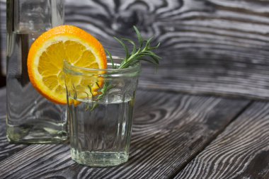 Bardaktaki cin. Bir dilim portakal ve biberiye ile süslenmiş. Yakınlarda bir içki şişesi var..