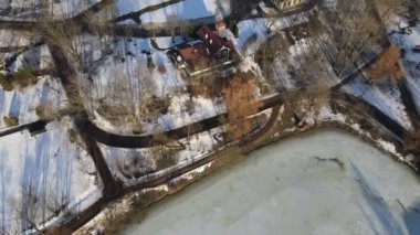 Kış parkı üzerinde uçuş. Kamera aşağıya doğru yönelir. Aşağıda buzla kaplı bir göl var. Parkın ortasında binalar görülebilir..