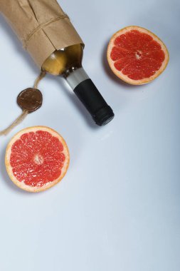 Alkol şişesi. Kağıda sarılmış. Greyfurtun yarı yarıya yakınında. Beyaz bir yüzeyde.