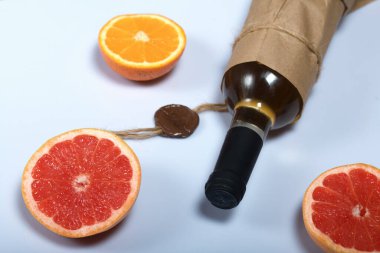 Alkol şişesi. Kağıda sarılmış. Yakınlarda bir portakal ve bir greyfurt var. Beyaz bir yüzeyde.