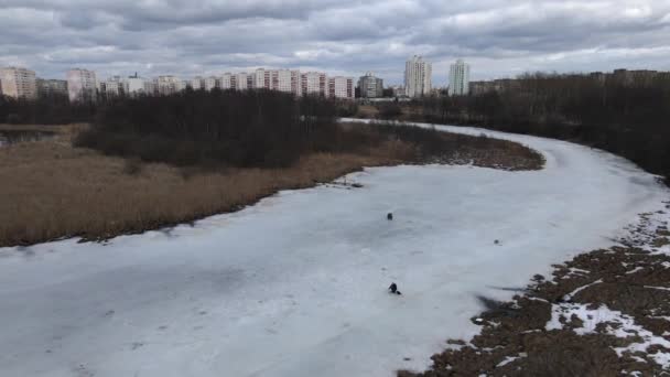 Létá nad řekou pokrytou ledem. Rybáři sedí na ledě. Zimní rybolov. Vícepodlažní budovy jsou viditelné na obzoru — Stock video