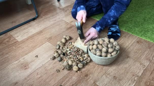 El hombre está rompiendo nueces. Golpea con un martillo en un bloque de madera. Nueces en el contenedor y en el suelo. — Vídeos de Stock