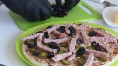 Bir adam pizzaya zeytin koyar. Yemek malzemeleri yakınlarda serili. Evde pizza yapmak. Yakın çekim..