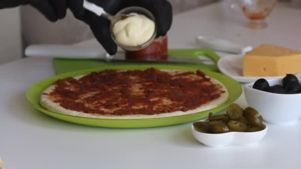 Un hombre extiende mayonesa sobre una base para una pizza untada con pasta de tomate. Los ingredientes de la cocina se exponen cerca. Haciendo pizza en casa. Primer plano de disparo. — Vídeo de stock