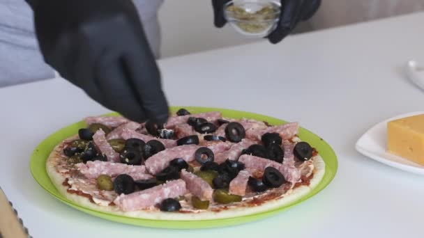 Un hombre rocía orégano sobre una base de pizza. Los ingredientes de cocción se establecen en él. Haciendo pizza en casa. Primer plano de disparo. — Vídeos de Stock