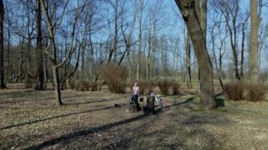 Bahar parkında bisiklet süren bir kız. Bir bankta oturuyor ve telefona bakıyor. Bisikleti yakınlarda. Hava fotoğrafçılığı bir İHA ile çekildi