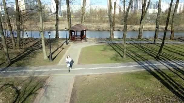 Mädchen auf einer Radtour zu Fuß im Frühlingspark. Mit dem Fahrrad die Gasse hinunter. Luftaufnahme mit einer Drohne — Stockvideo