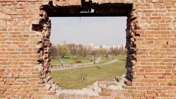 Ruínas de um velho moinho em Loshitsky Park, Minsk, Bielorrússia. Voando através da abertura da janela de um edifício destruído. Perto do gramado está uma menina segurando uma bicicleta em suas mãos. — Vídeo de Stock