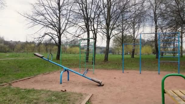 Volando en el parque infantil en el parque de la ciudad de primavera. Entre los equipos deportivos de metal. Equipo de ejercicio retro en el parque infantil. — Vídeos de Stock