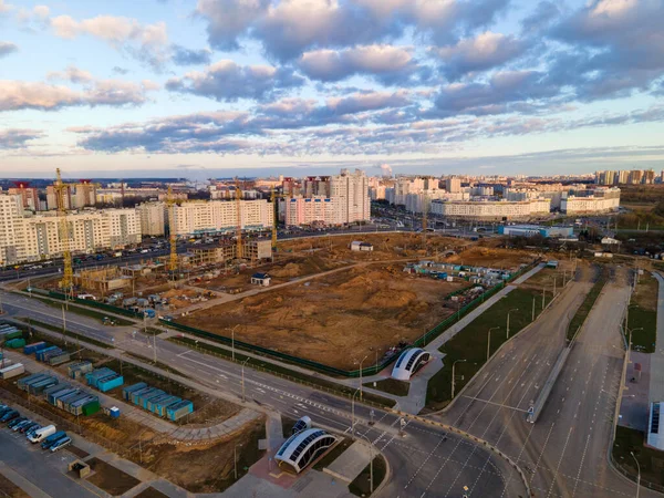 Construction site at dawn. Claimed multi-storey houses are visible. Construction cranes and neighboring urban quarters. Panoramic aerial photography.