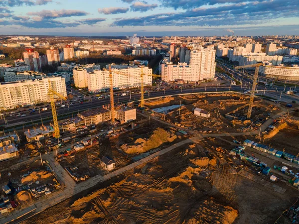 Construction site at dawn. Claimed multi-storey houses are visible. Construction cranes and neighboring urban quarters. Panoramic aerial photography.