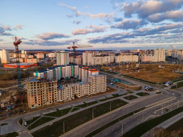 Construction site at dawn. Claimed multi-storey houses are visible. Construction cranes and neighboring urban quarters. Panoramic aerial photography.