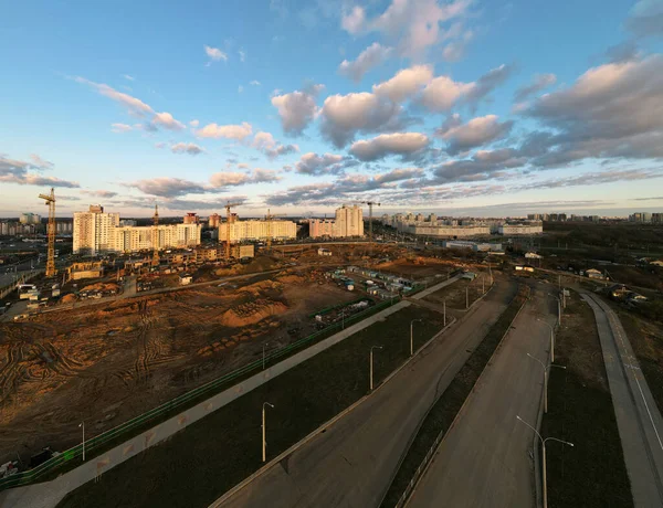 Construction site at dawn. Claimed multi-storey houses are visible. Construction cranes and neighboring urban quarters. Panoramic aerial photography.