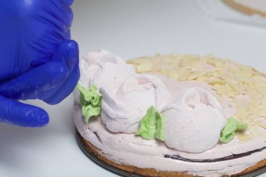 Bir kadın lokum keki hazırlar. Gül yapraklarında marşmelovdan yeşil yapraklar yapıyor. Maske ve eldivenle çalışıyor..